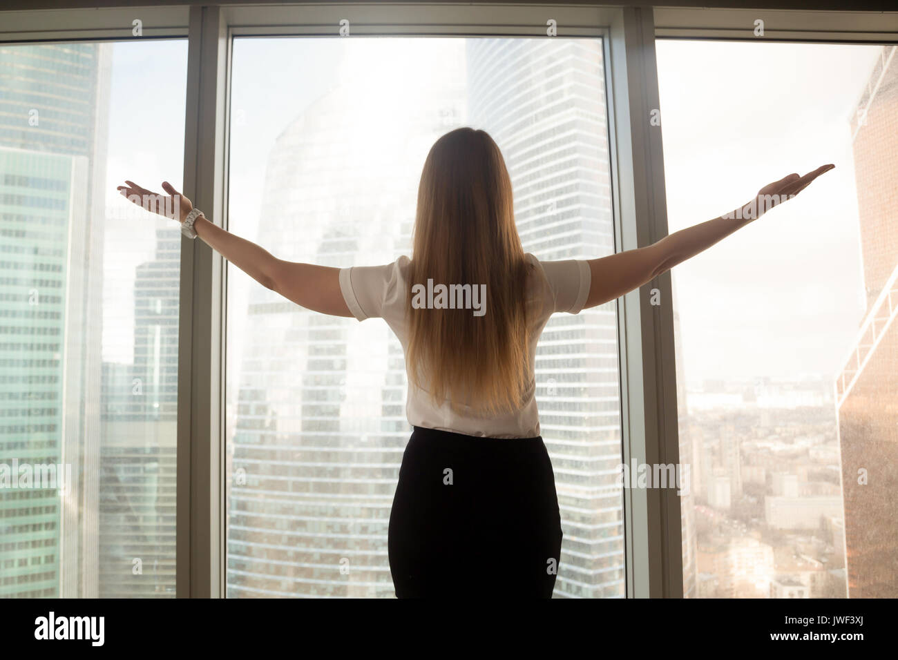Fiducioso imprenditrice diffondendo le mani in piedi alla finestra grande, Foto Stock