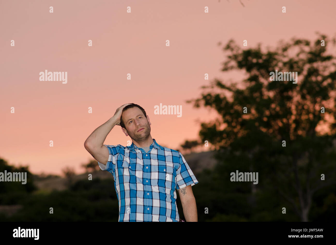 Uomo con una mano sulla sua testa a pensare a cosa succede domani al tramonto. Foto Stock