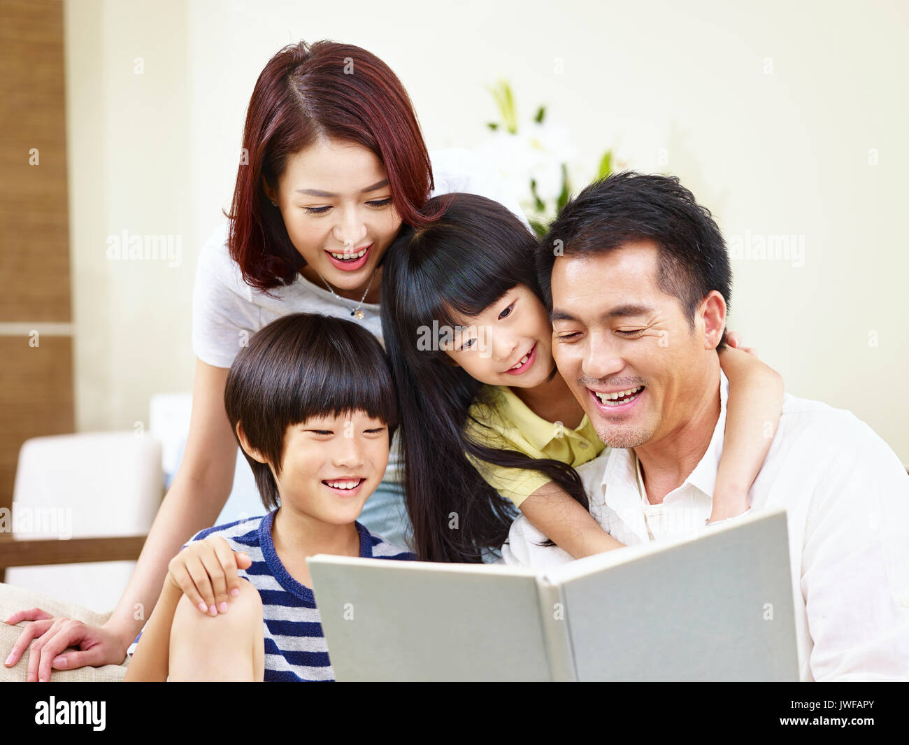 Felice famiglia asiatica con due bambini seduti sul divano a leggere un libro insieme. Foto Stock