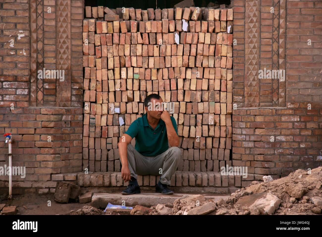 Uomo seduto di fronte ad un mucchio di mattoni nella città vecchia Kashgar Foto Stock