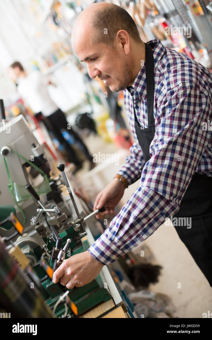 Uomo maturo nel lavoro di fabbro e rendendo i duplicati di chiavi Foto Stock
