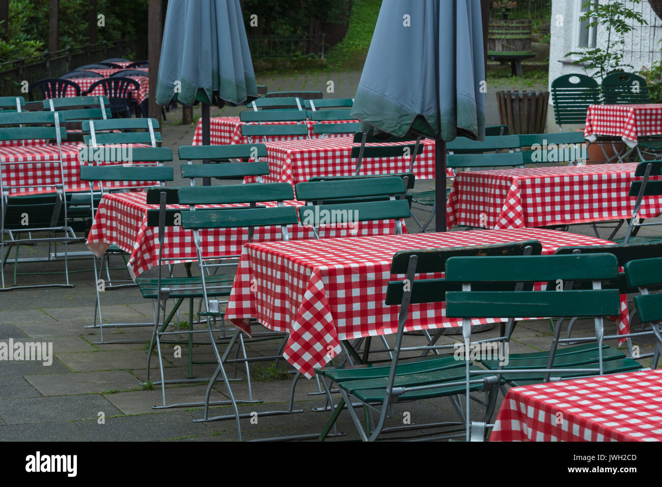 Svuotare le tabelle di birra con il rosso tovaglia bianca e verde con sedie in legno in un pubblico giardino della birra. Foto Stock