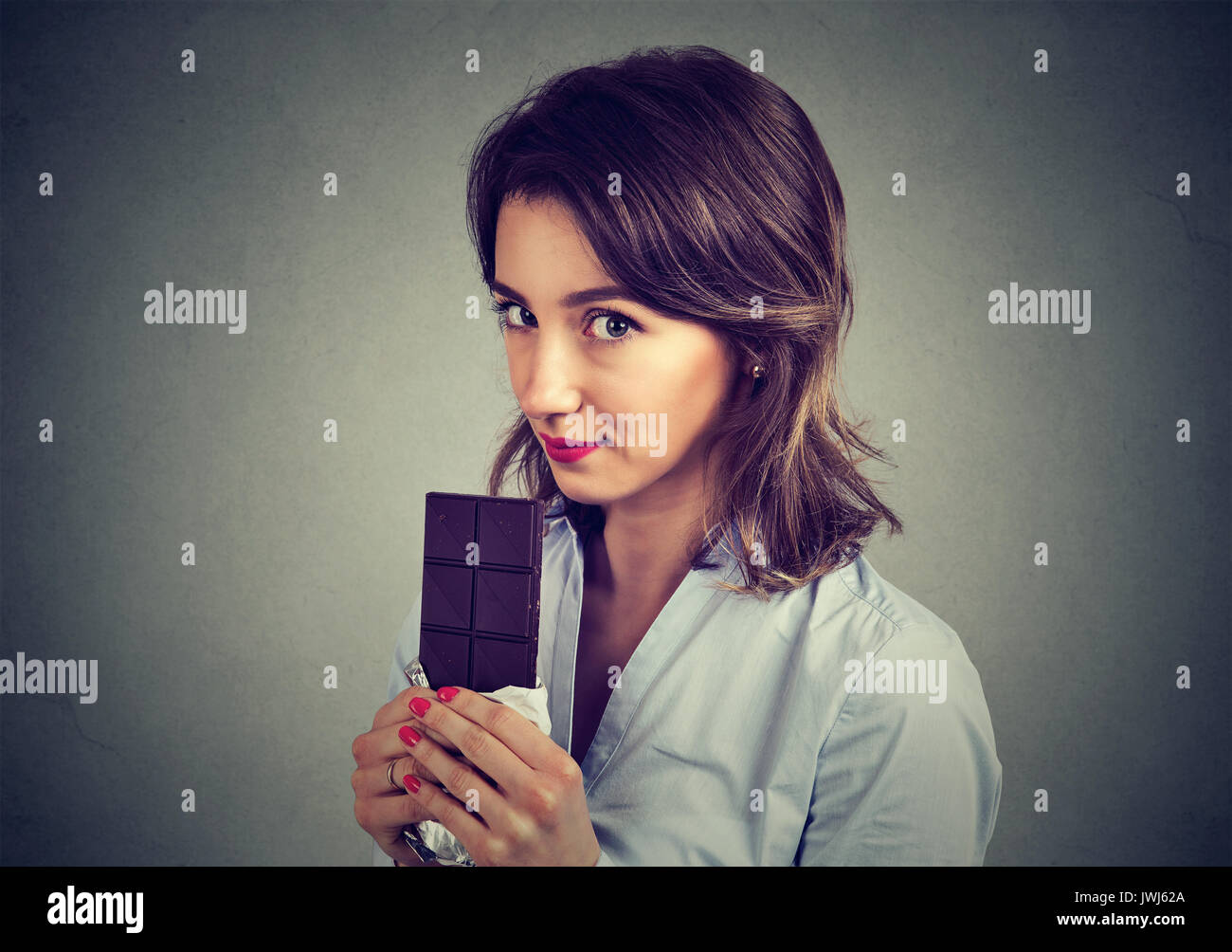 Closeup ritratto della cute giovane donna di mangiare il cioccolato isolati su sfondo grigio Foto Stock