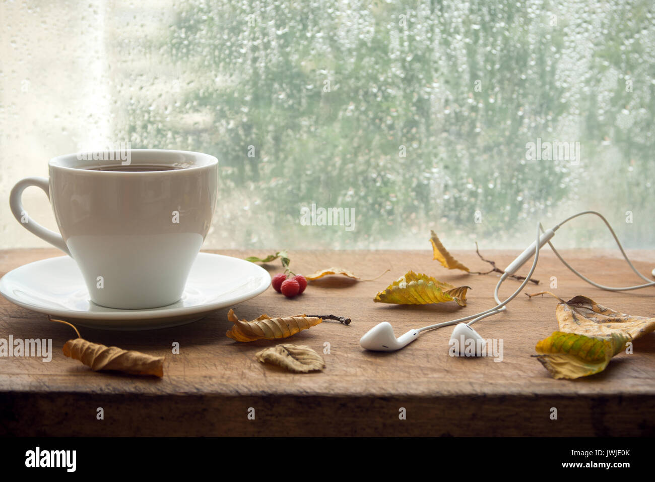 Tazza di caffè o di tè, smartphone e gli auricolari con foglie di autunno vicino a una finestra. In autunno il concetto di playlist. Musica Autunno per giorni di pioggia. Foto Stock