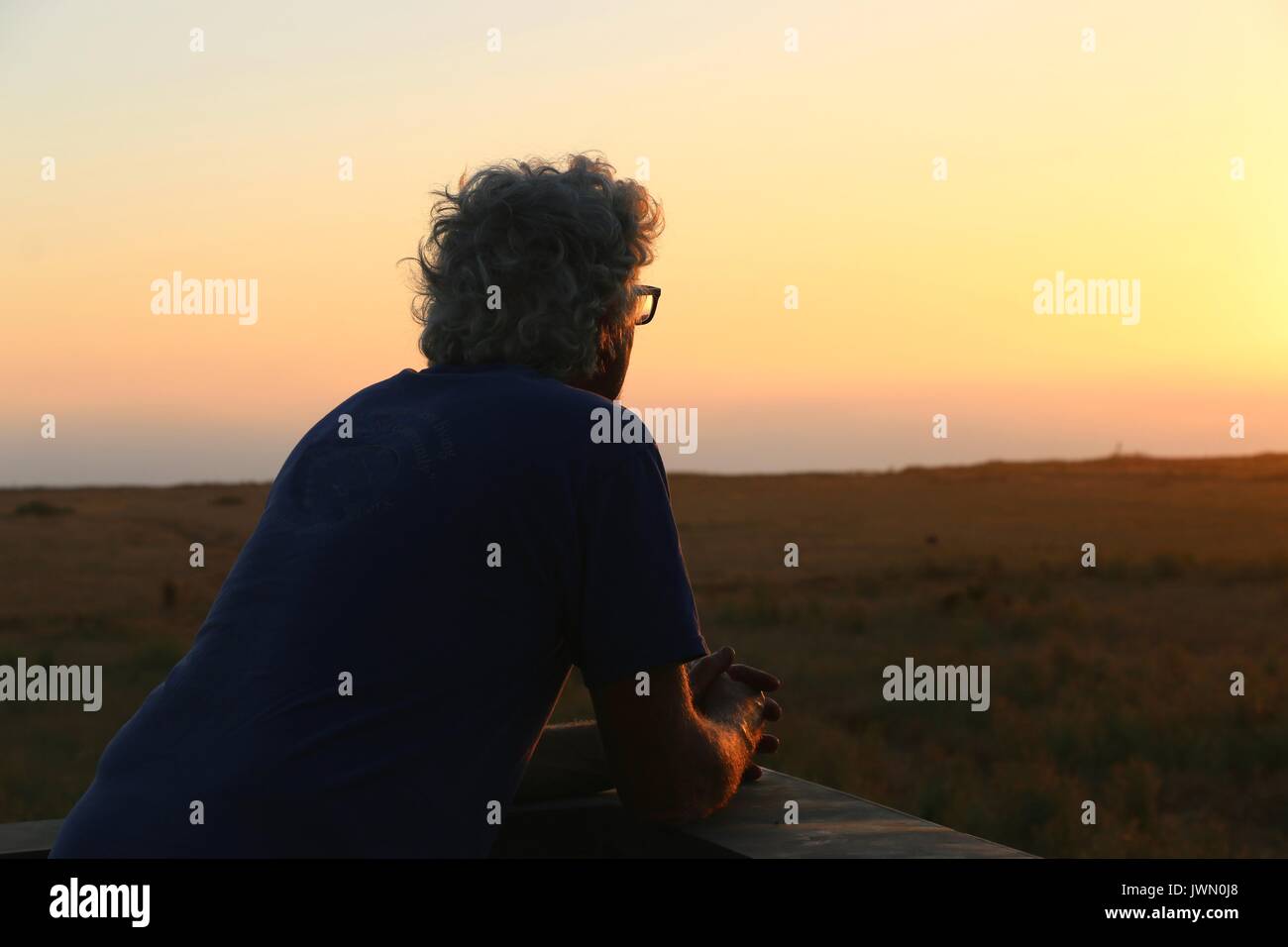 Senior uomo guarda il tramonto in un momento di pacifica solitudine. Foto Stock