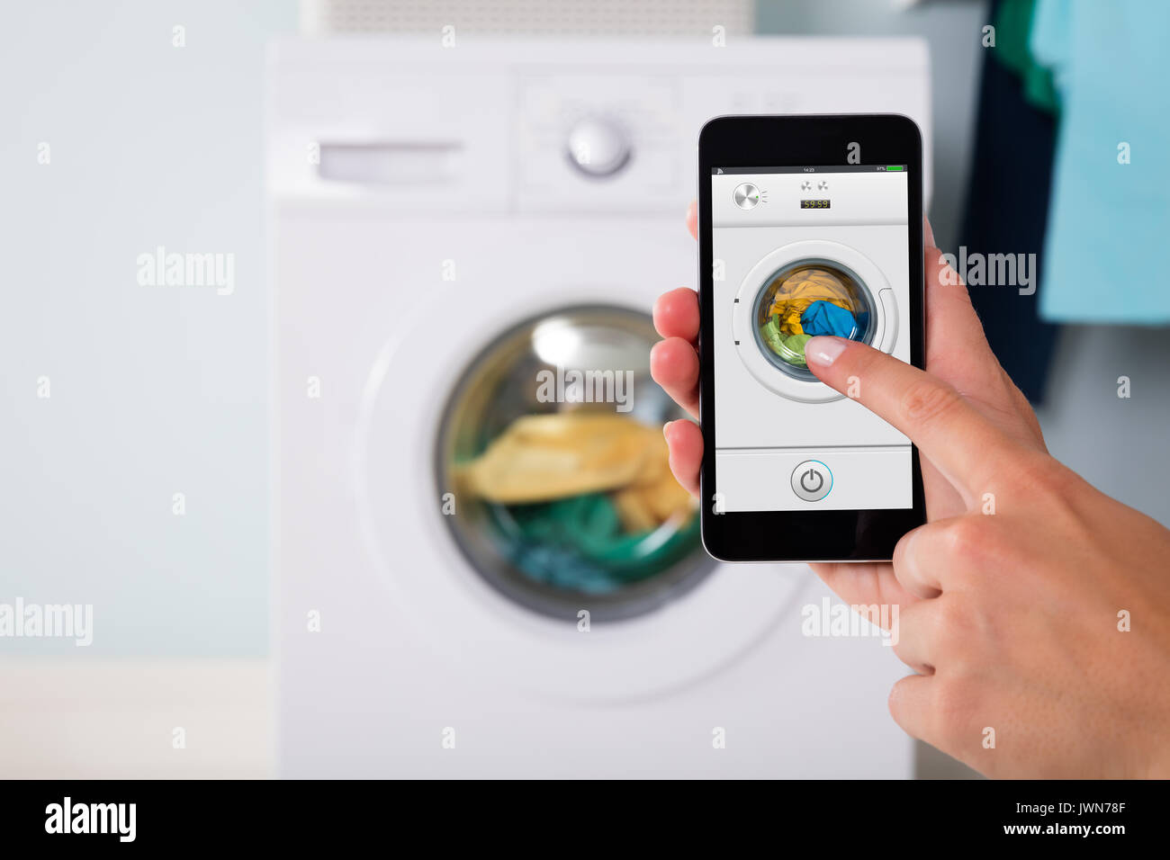Close-up di persona a mano di funzionamento della macchina di lavaggio tramite telefono cellulare utilizzando l'app Foto Stock