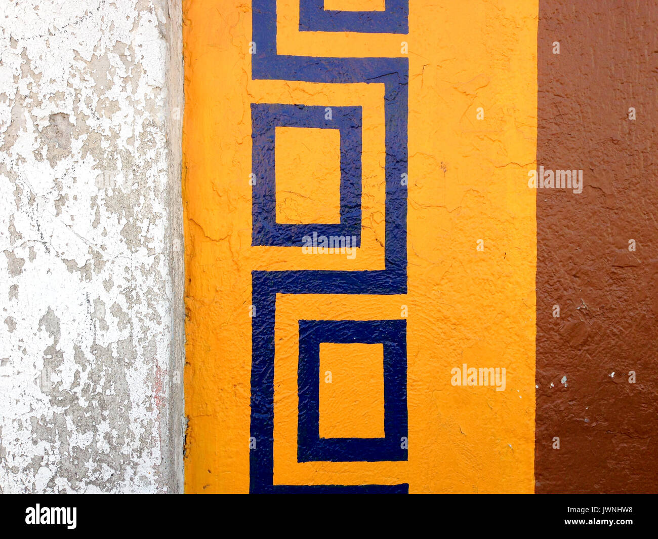 Colorato schema di ripetizione confine dipinta su un muro esterno con un motivo blu su una cornice gialla con vernice marrone a fianco, grungy sezione di parete Foto Stock
