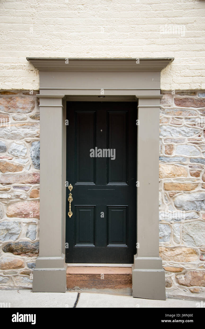 Vecchia dipinta di nero porta in legno con maniglia in ottone in architettura coloniale con un semplice pietra intagliata surround impostato in una naturale parete di roccia modifica a b Foto Stock