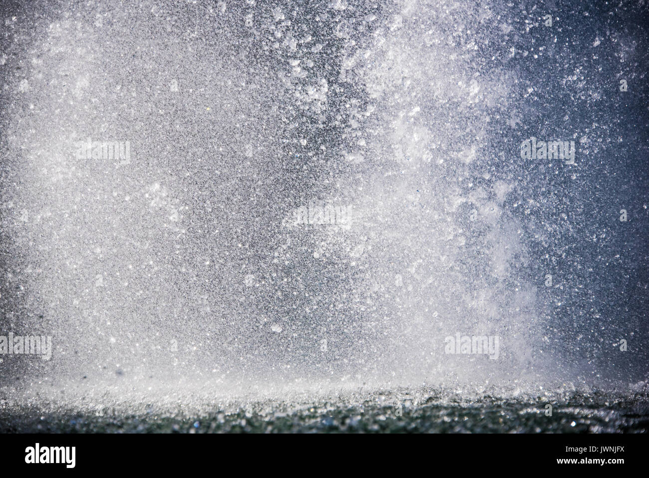 Movimento congelato le goccioline di acqua in una fontana spray al di sopra di un laghetto brilla al sole estivo per una rinfrescante sfondo Foto Stock