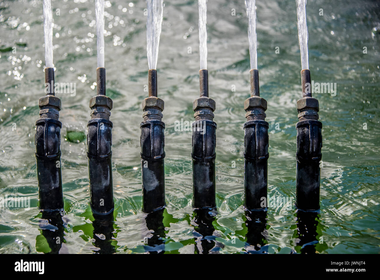 Fila di sei alta pressione ugelli di metallo su una fontana dei getti di irrorazione di acqua in aria in un display ornamentali, vista ravvicinata Foto Stock