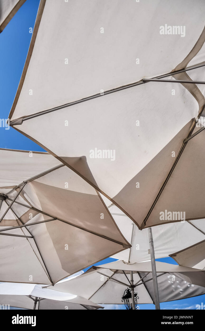 Guardando in alto in un gruppo di tela bianca spiaggia ombrelloni vicino insieme sotto un sole estivo blu cielo in un concetto di resort, vacanze e viaggi Foto Stock