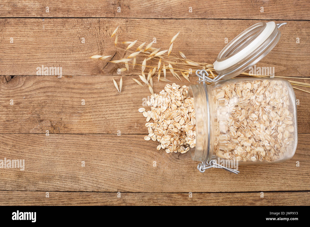 Fiocchi di avena in un barattolo di vetro e oat orecchio sul tavolo di legno vista dall'alto. Non cotti i fiocchi d'avena Foto Stock