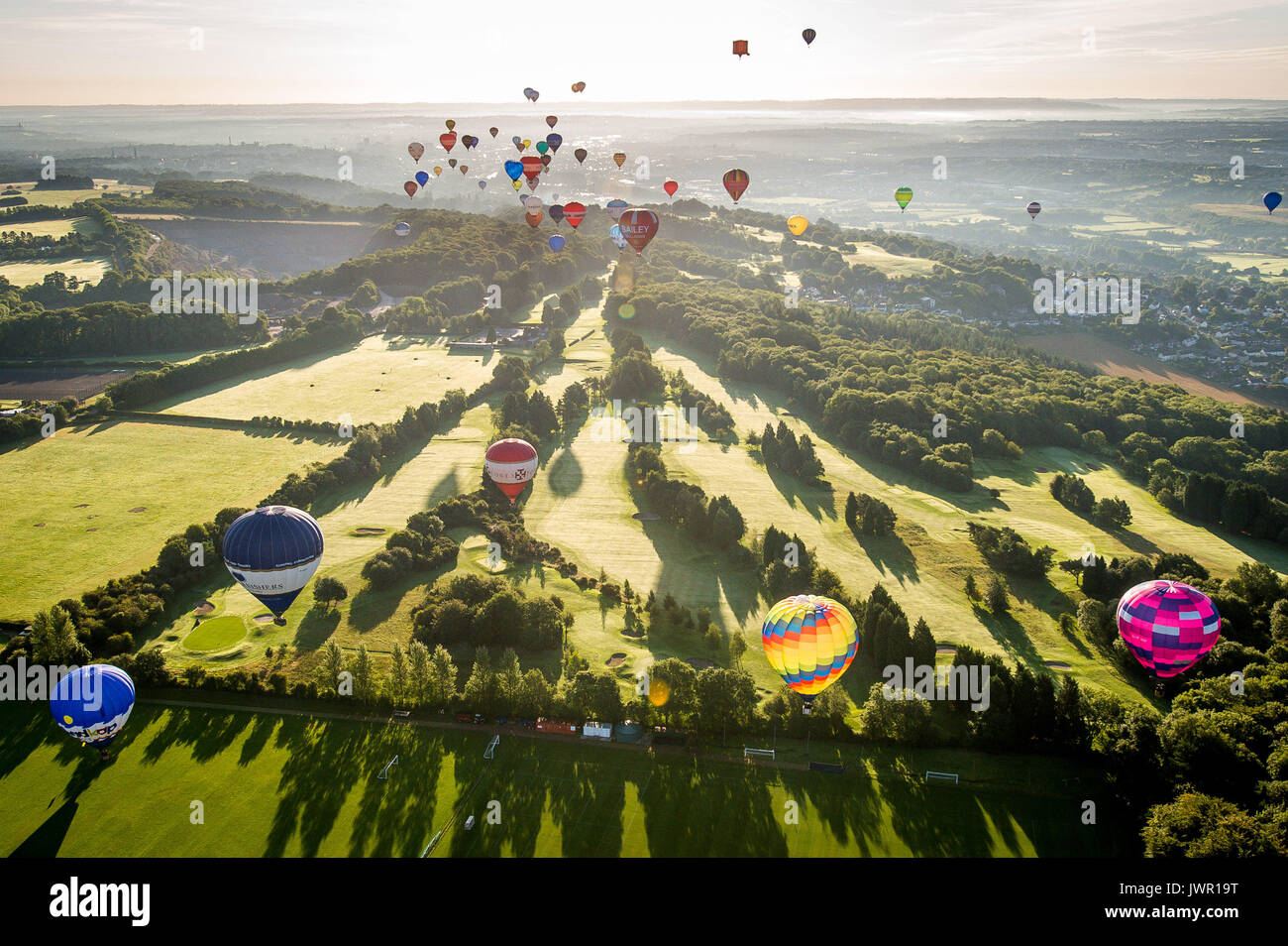 I palloncini ad aria calda si librano su un campo da golf vicino a Long Ashton, Bristol, durante l'ascesa di massa, dove i palloncini provenienti da tutto il mondo si riuniscono ad Ashton Court, Bristol, per partecipare alla Fiesta Internazionale della mongolfiera di Bristol. Foto Stock