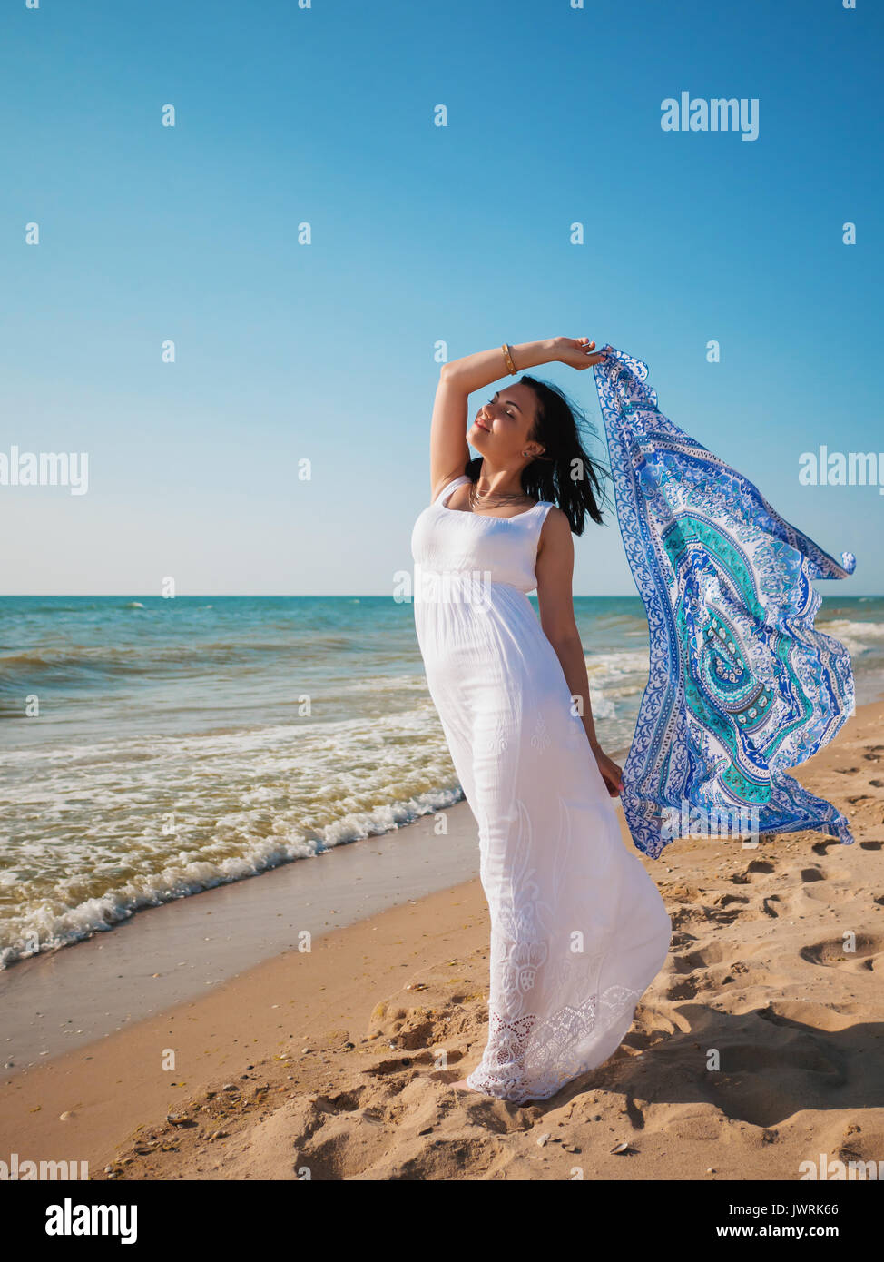 I giovani zingari brunette Girl indossando maxi bianco abito lungo in piedi  sul mare o oceano beach con mandala foulard di seta in mani. Bohemian stile  di abbigliamento Foto stock - Alamy