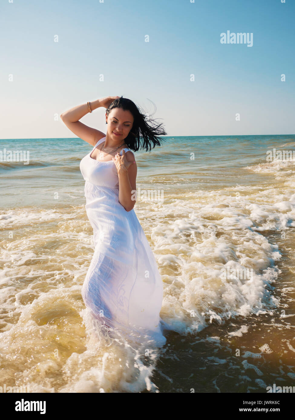 I giovani zingari brunette Girl indossando maxi bianco abito lungo in piedi  al mare o oceano con onde e schiuma. Bohemian stile di abbigliamento. Stile  Boho Foto stock - Alamy