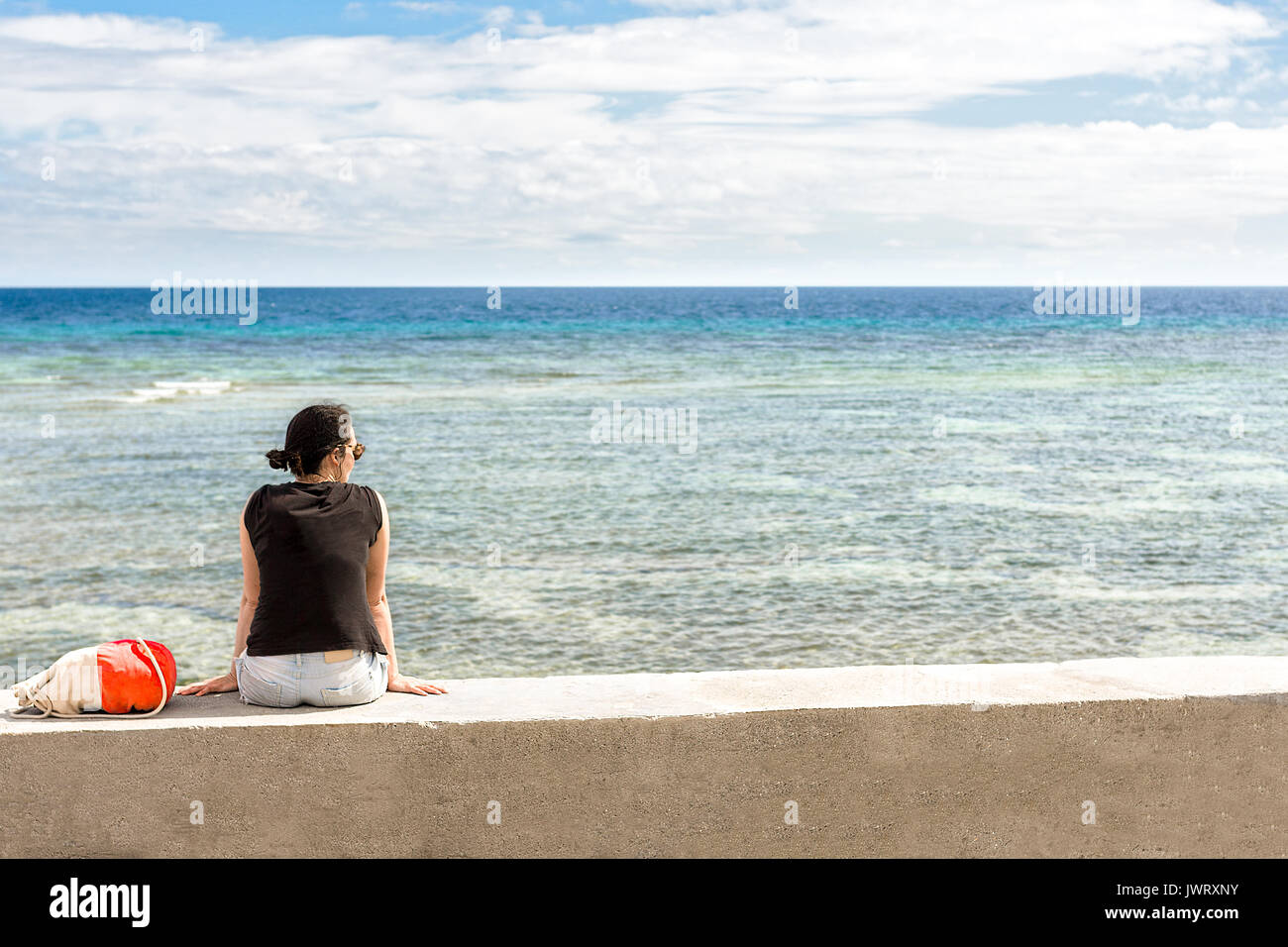 Femmina solitario seduto a guardare oltre un tropicale mare cristallino su un muro di cemento Foto Stock