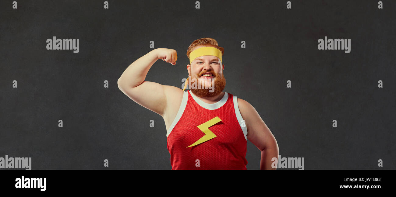 Funny fat man in abbigliamento sportivo mostra una mano con i muscoli bicipite Foto Stock