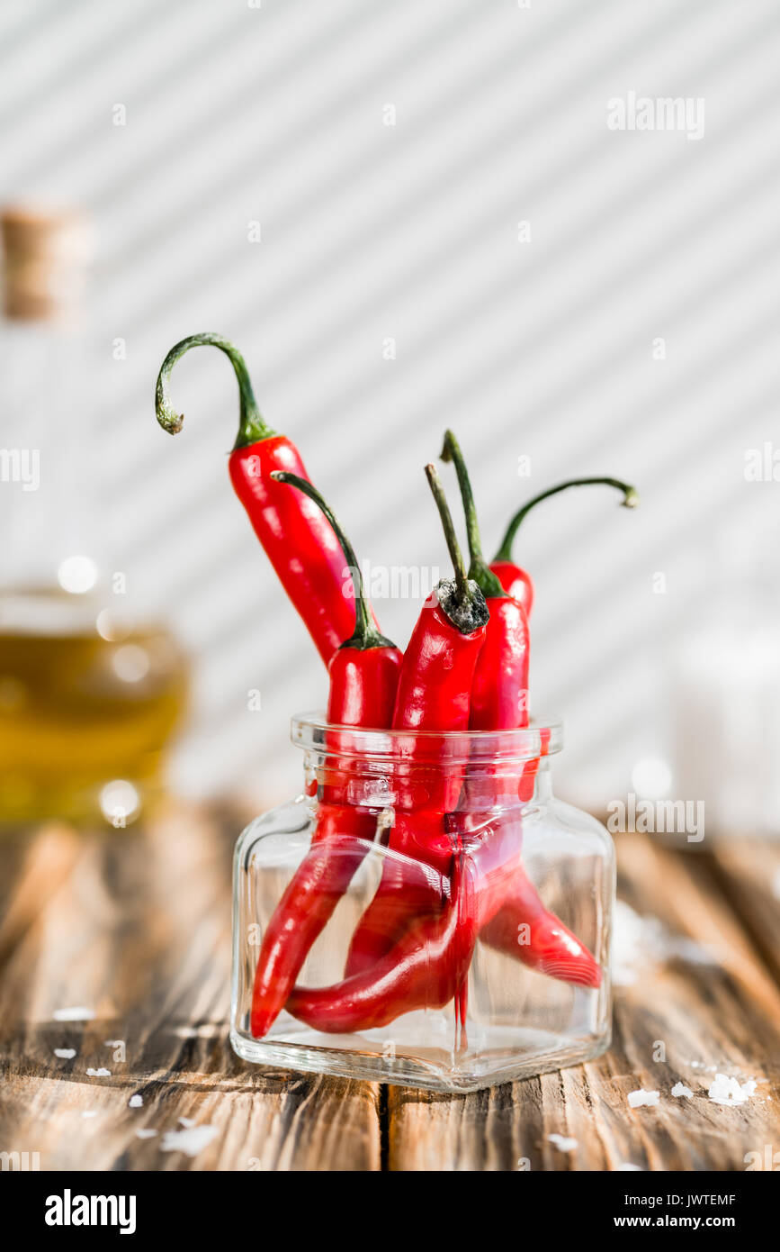 Peperoncino rosso in un barattolo di vetro, sale marino e olio di oliva su un tavolo di legno. Dura la luce del mattino Foto Stock