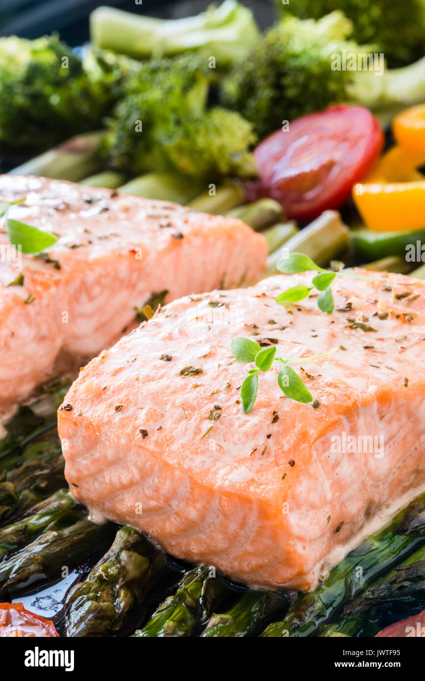 Due pezzi di filetto di salmone al forno su asparagi verdi, pepe,  pomodorini e broccoli sul vassoio da forno guarnito con timo fresco. Pranzo  cucinato Foto stock - Alamy