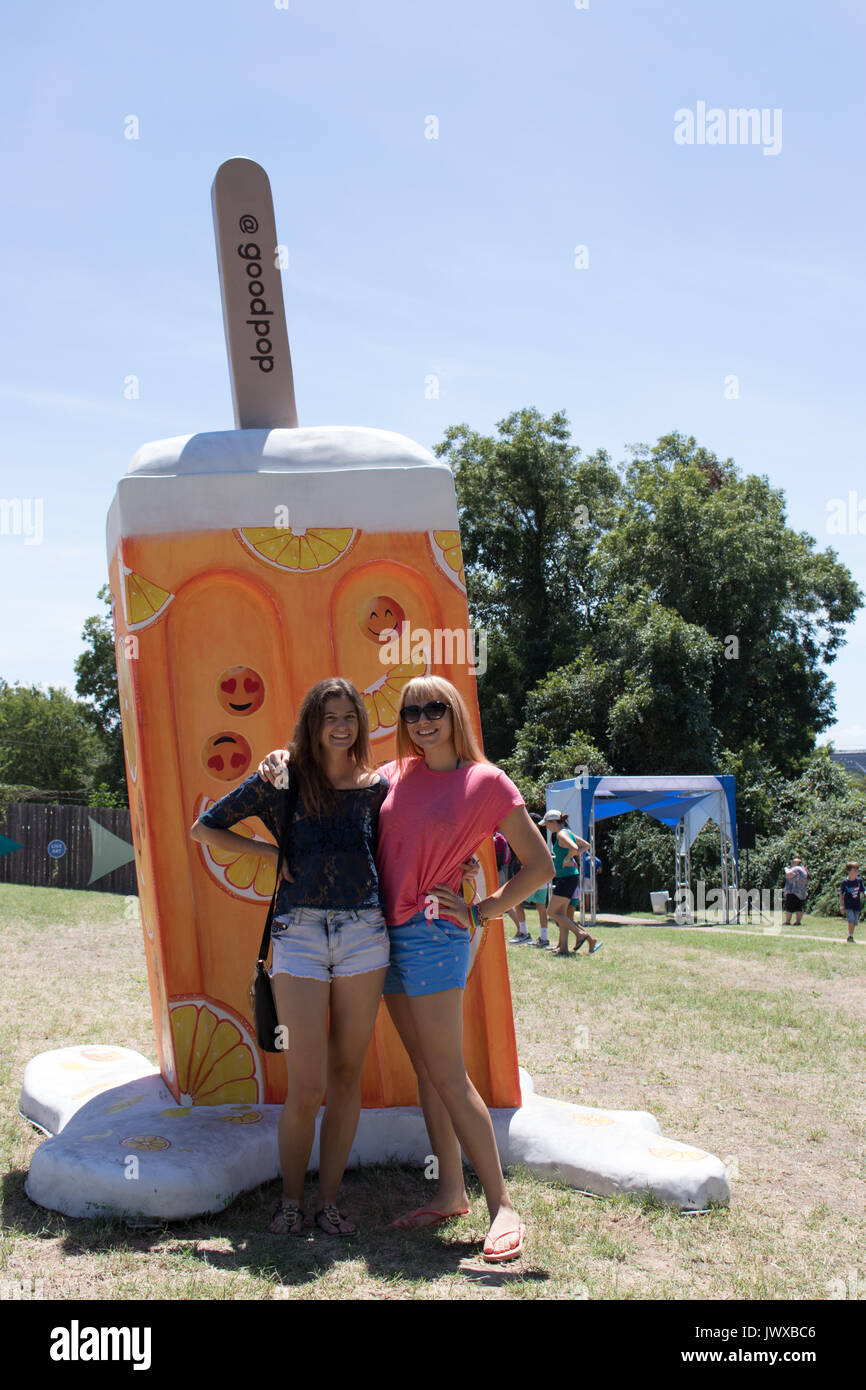 Due giovani donne in piedi accanto a un modello di grandi dimensioni di un arancio ghiaccioli all'aperto presso la Austin Gelato Festival. Alberi e cielo blu in background. Foto Stock