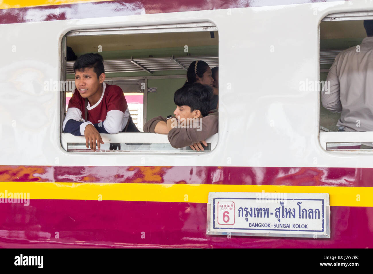 Giovani uomini guardando fuori dalla finestra di un treno fermo, Hua Lamphong stazione ferroviaria, Bangkok, Thailandia Foto Stock