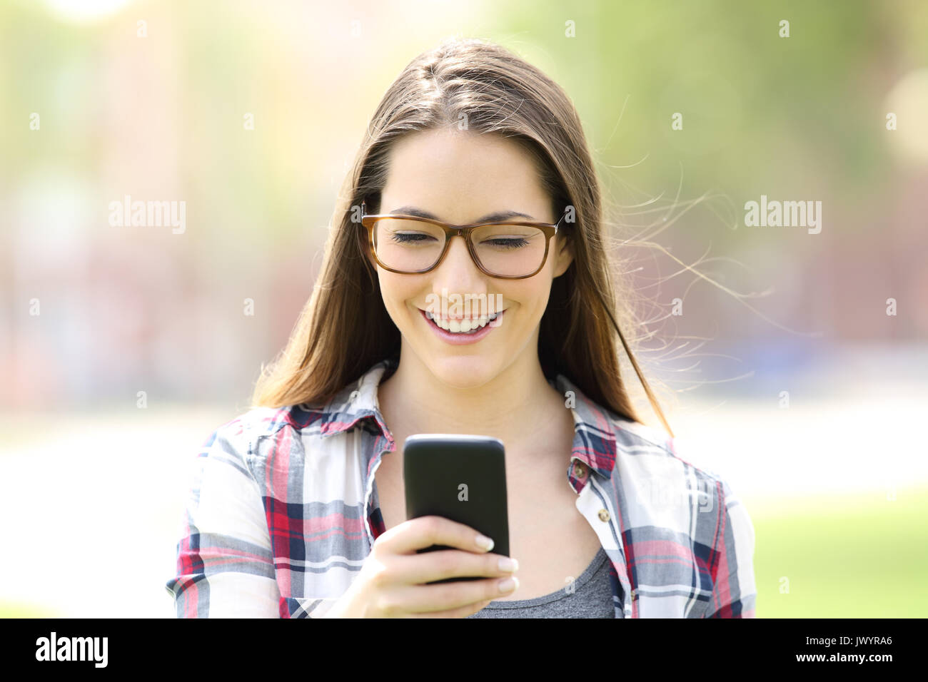 Vista frontale di una singola ragazza indossando occhiali controllo telefono cellulare in strada Foto Stock