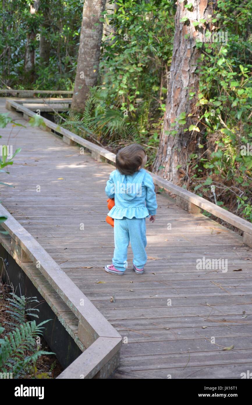 Una femmina di bambino in una tuta blu a piedi attraverso il parco alberato . Foto Stock