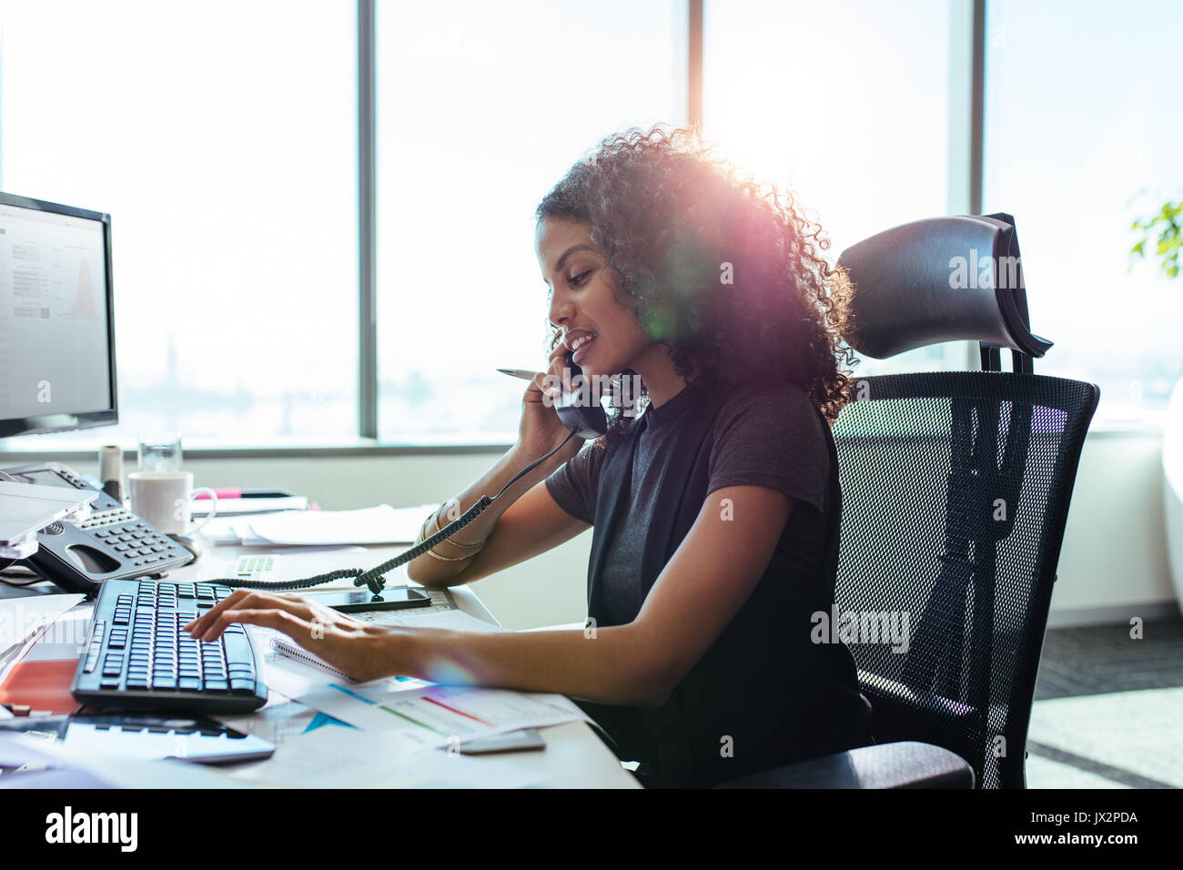 Donna imprenditore occupato con il suo lavoro in ufficio. Giovane donna di parlare telefonicamente mentre si lavora sul computer alla sua scrivania. Foto Stock