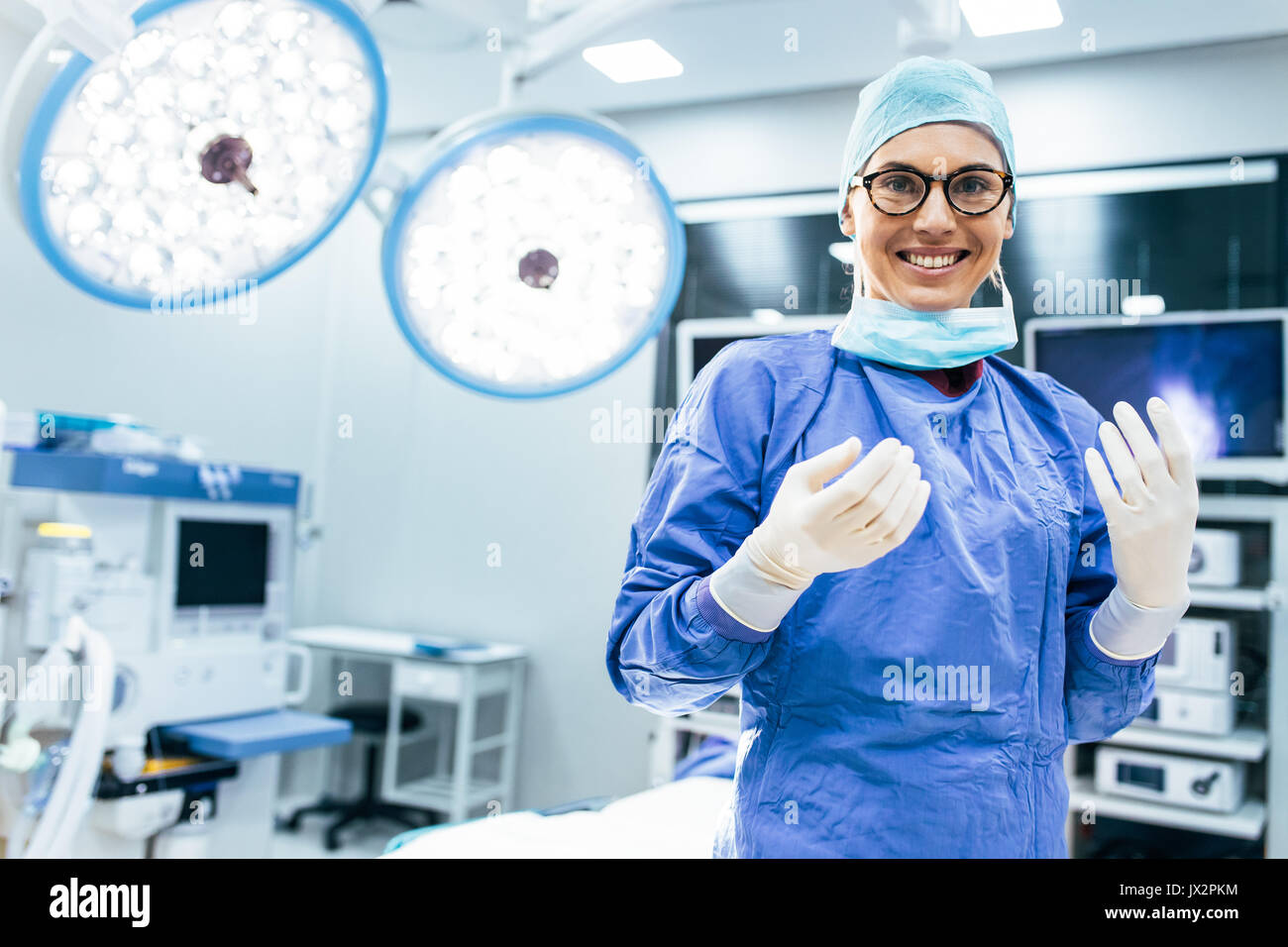 Ritratto di donna felice chirurgo in piedi in sala operatoria, pronto a lavorare su un paziente. Femmina lavoratore medico chirurgico uniforme nel teatro di funzionamento Foto Stock