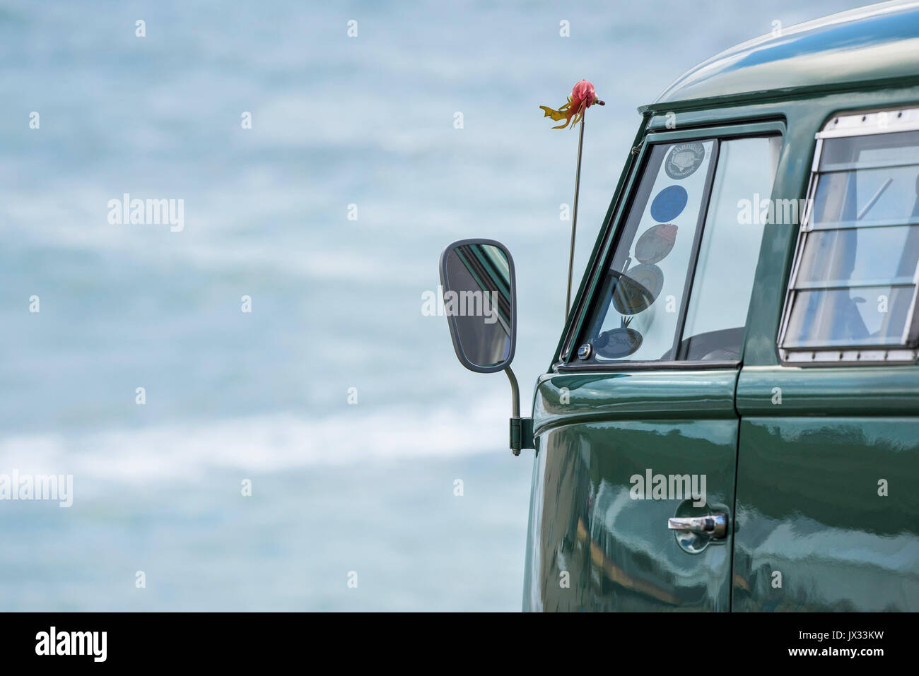 Dello specchietto retrovisore sul lato di un vintage VW camper parcheggiato affacciato sul mare. Foto Stock