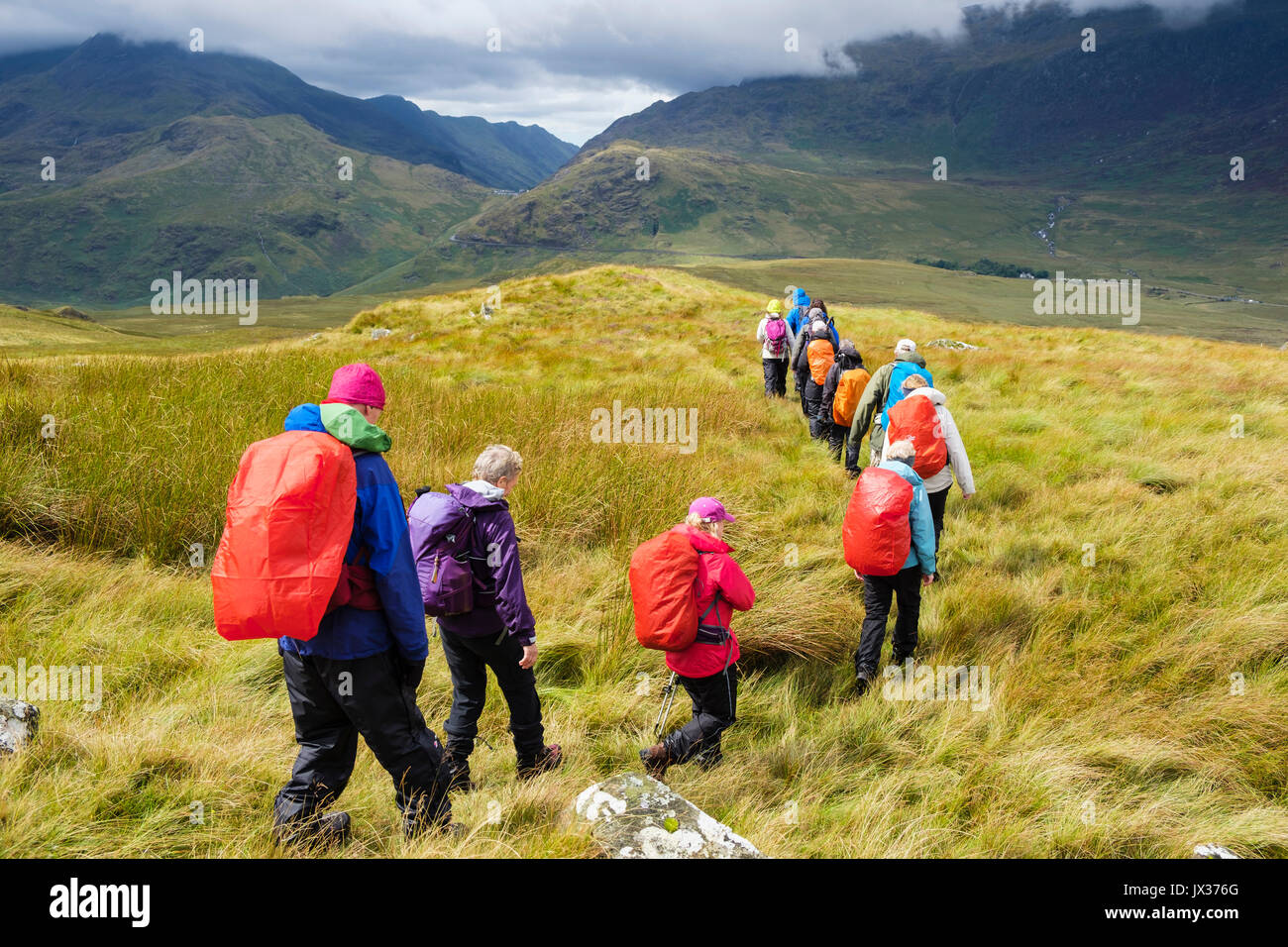 Persone che indossano l'orecchio di pioggia su Carnedd y Cribau trekking fino a Pen Y Gwryd al sole dopo pioggia tempo bagnato in montagne di Snowdonia. Galles Regno Unito Foto Stock