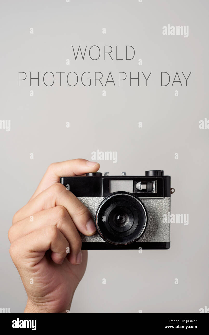 Primo piano della mano di un uomo giovane con un retrò fotocamera a pellicola e il testo world photography giornata contro un sfondo bianco Foto Stock