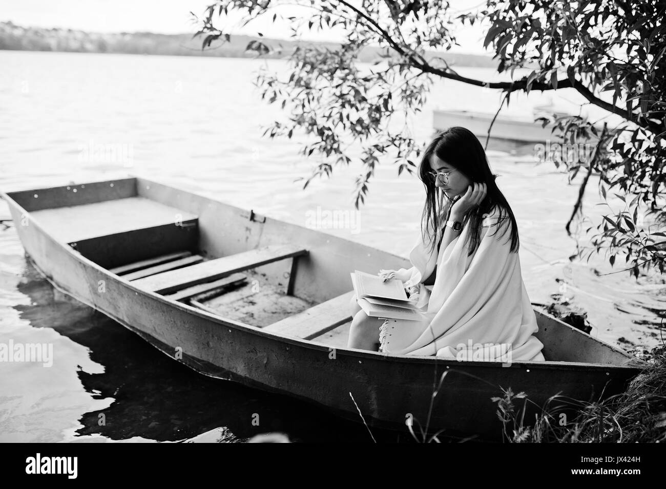 Ritratto di una donna attraente vestita di nero a pois, vestito scialle bianco e degli occhiali per leggere un libro in una barca sul lago. Foto in bianco e nero. Foto Stock