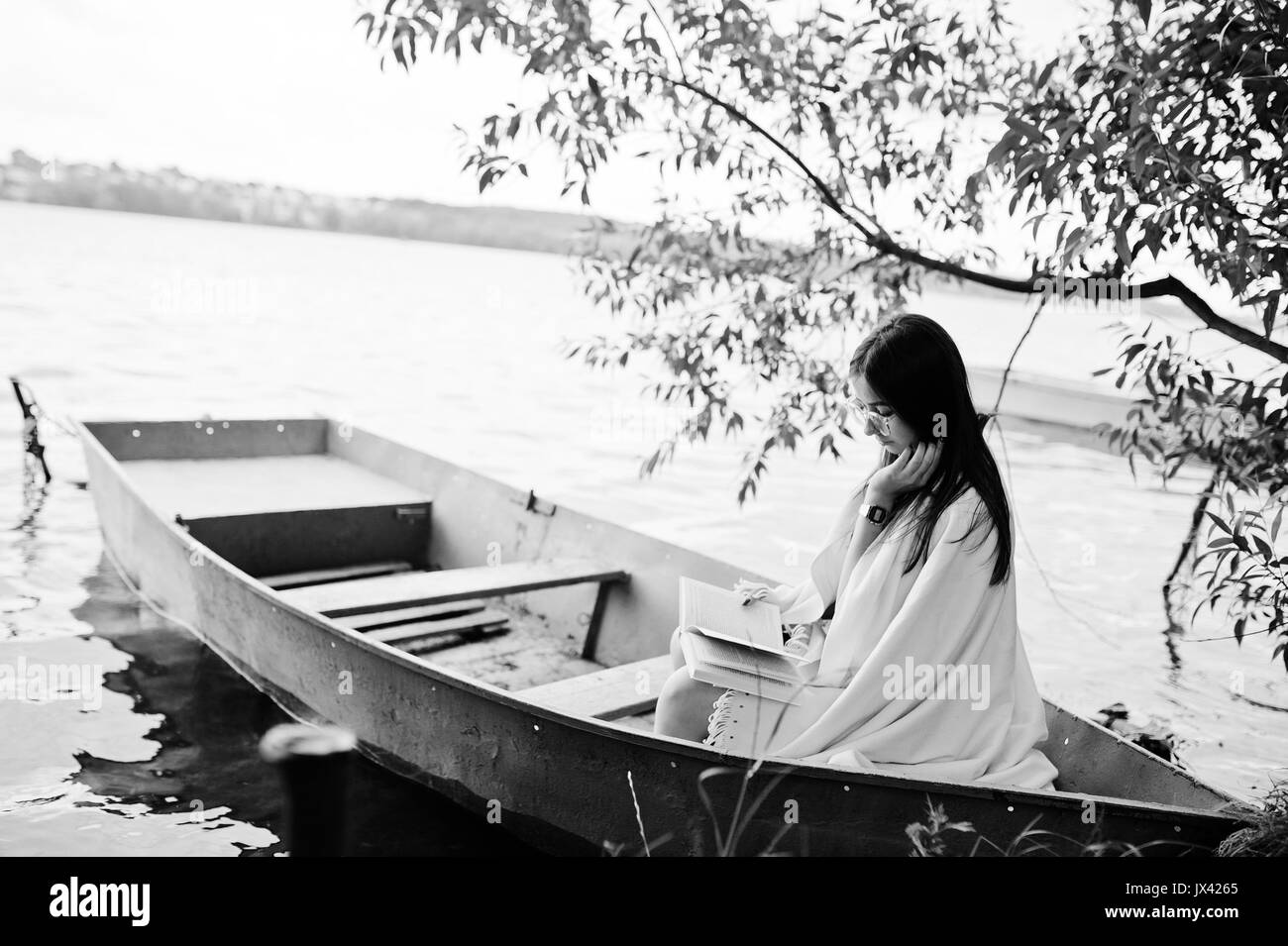Ritratto di una donna attraente vestita di nero a pois, vestito scialle bianco e degli occhiali per leggere un libro in una barca sul lago. Foto in bianco e nero. Foto Stock