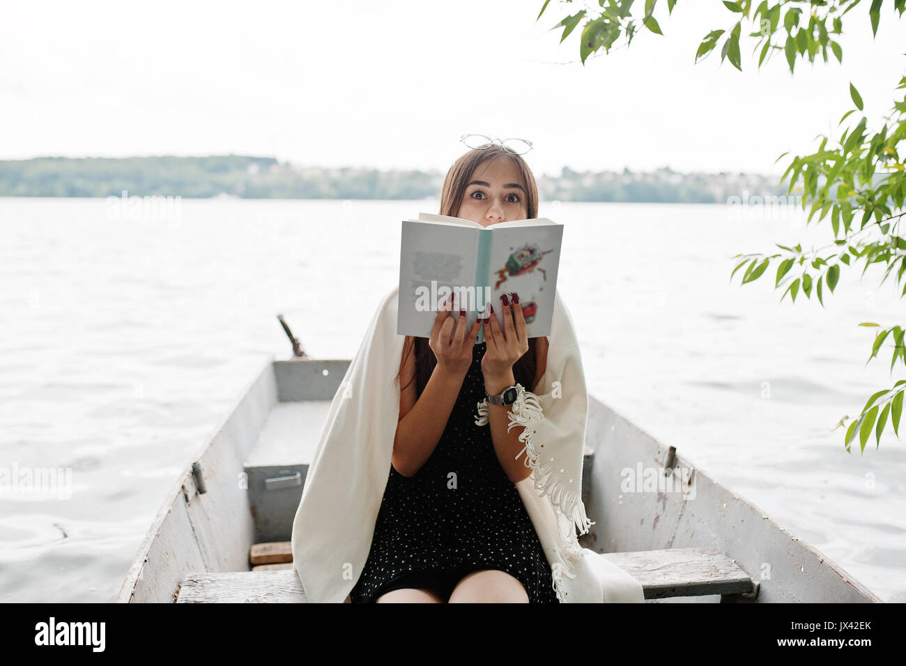 Ritratto di una donna attraente vestita di nero a pois, vestito scialle bianco e degli occhiali per leggere un libro in una barca sul lago. Foto Stock