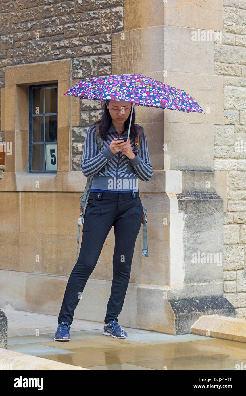 Donna che usa il telefono cellulare al riparo sotto un ombrello in una giornata piovosa bagnata a Oxford, Oxfordshire UK nel mese di agosto Foto Stock