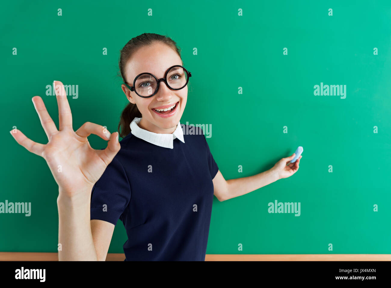 Studente sorridente mostra gesto okay e punti a qualcosa. Foto di teen vicino a lavagna, il concetto di istruzione Foto Stock