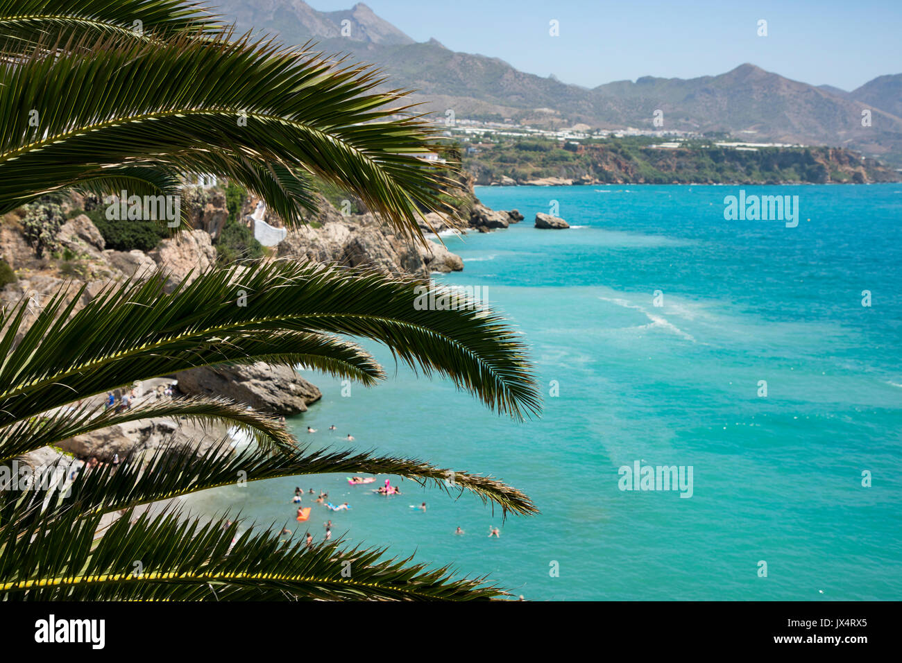 La spagnolo Costa d'estate con la gente sulla spiaggia nell'acqua blu e la montagna in background e un albero di palma in primo piano Foto Stock