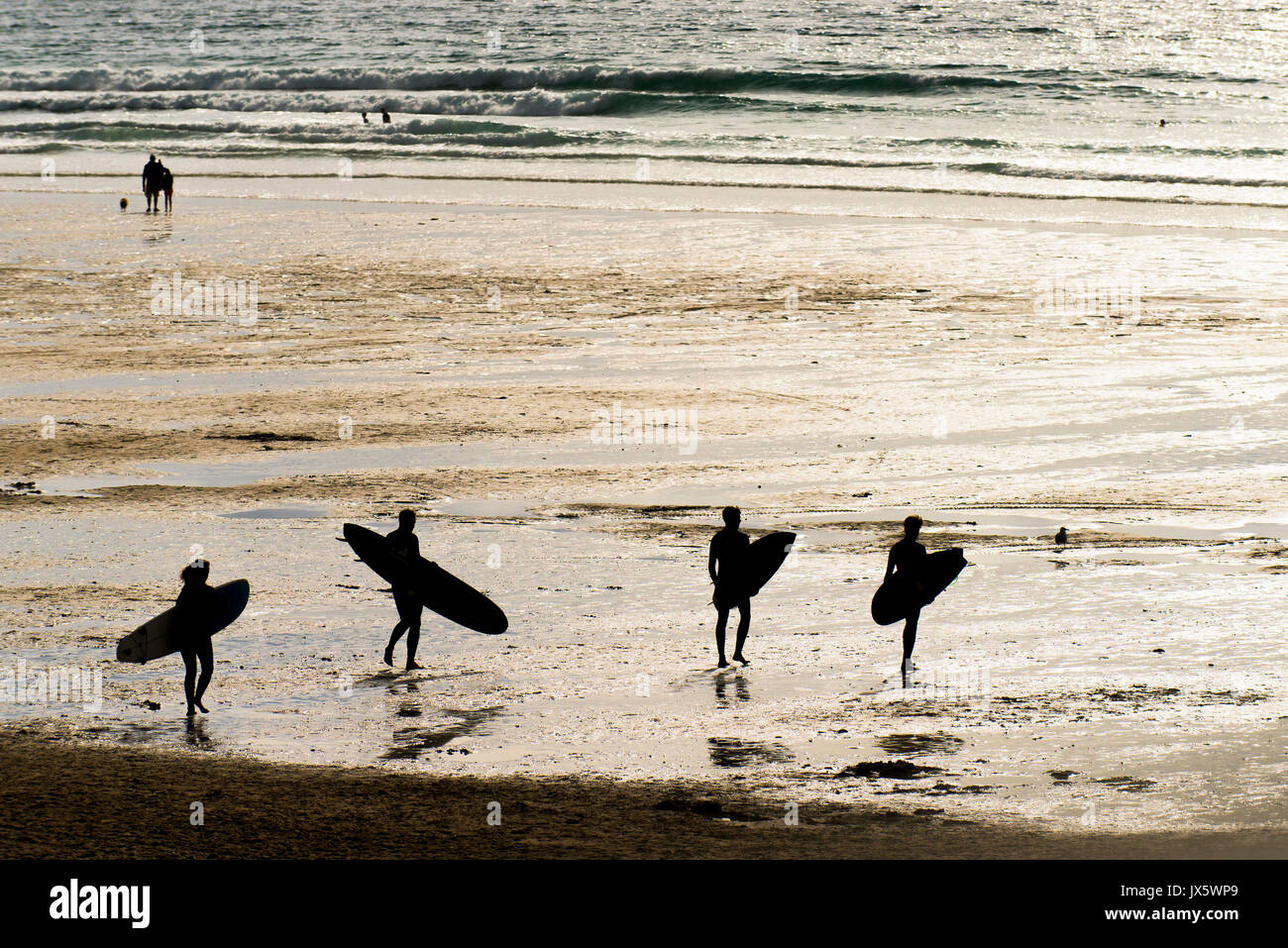 Quattro surfers visto in silhouette come essi portano le loro tavole da surf su Fistral Beach in Newquay, Cornwall. Foto Stock
