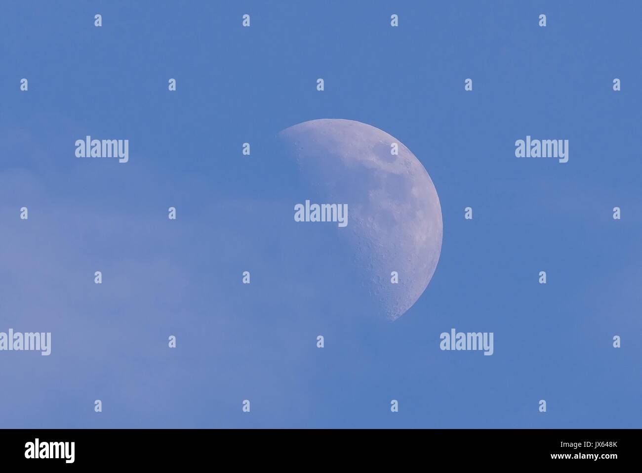 Foto orizzontale di mezza luna catturati durante le ore diurne. Poche nuvole sono sulla foto accanto al satellite. Cielo azzurro è in background. I crateri Foto Stock