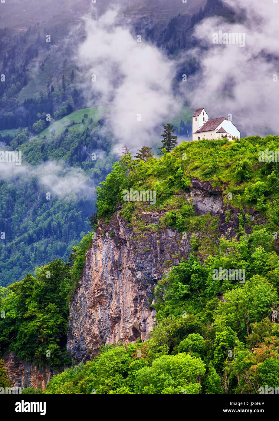 Piccola chiesa bianca su una roccia nelle alpi svizzere in una nebbiosa mattina, Svizzera Foto Stock
