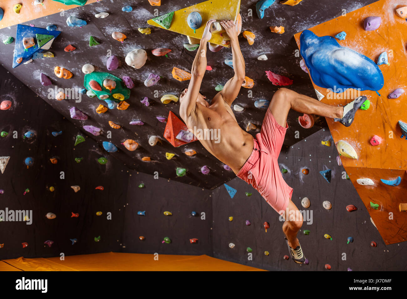 Giovane uomo bouldering in piscina palestra di arrampicata, cercando di risolvere il problema stimolante Foto Stock