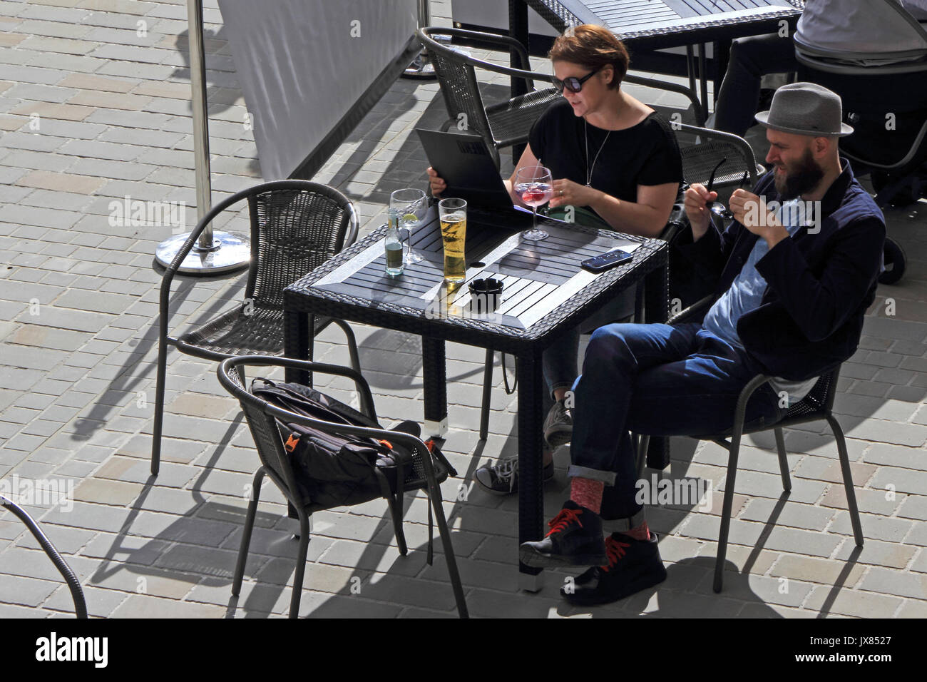Giovane godendo un sole estivo mentre si utilizza il computer e avente le bevande a tavola al di fuori dei bar. Foto Stock