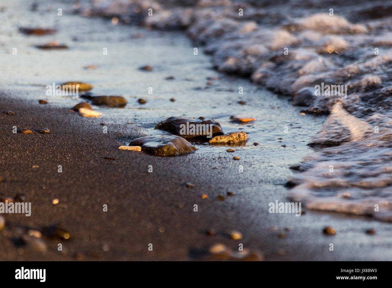 Una foto vicina di un lago, con i dettagli di bolle di acqua e un po' di pietre e ciottoli sulla sabbia Foto Stock