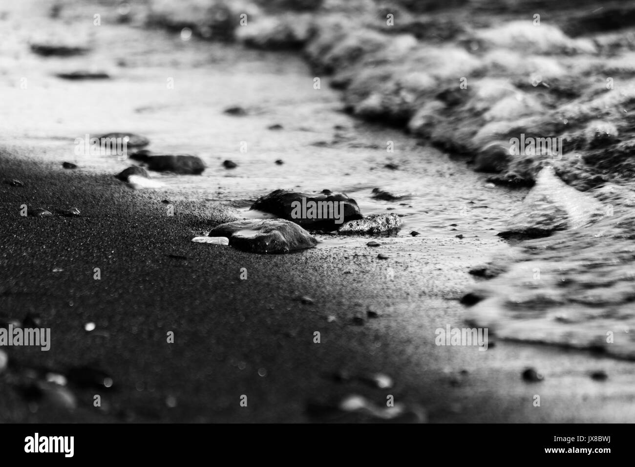Una foto vicina di un lago, con i dettagli di bolle di acqua e un po' di pietre e ciottoli sulla sabbia Foto Stock