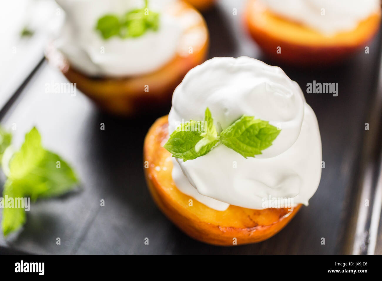 Grigliata peachs organico con la panna montata e guarnita con menta fresca. Foto Stock