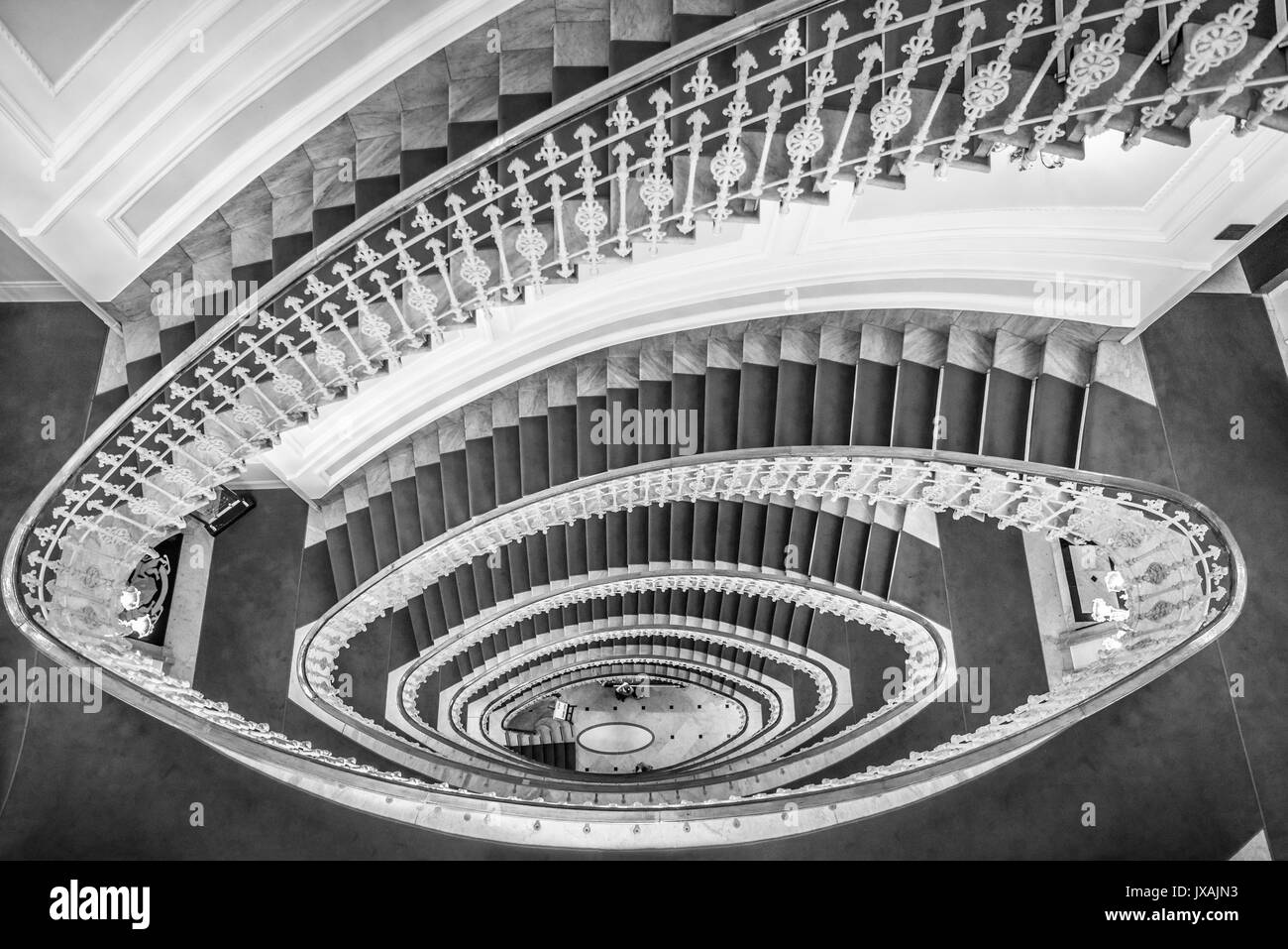 Immagine monocromatica di scale a spirale realizzata in marmo con un tappeto rosso e un elegante ringhiera, vista da sopra Foto Stock