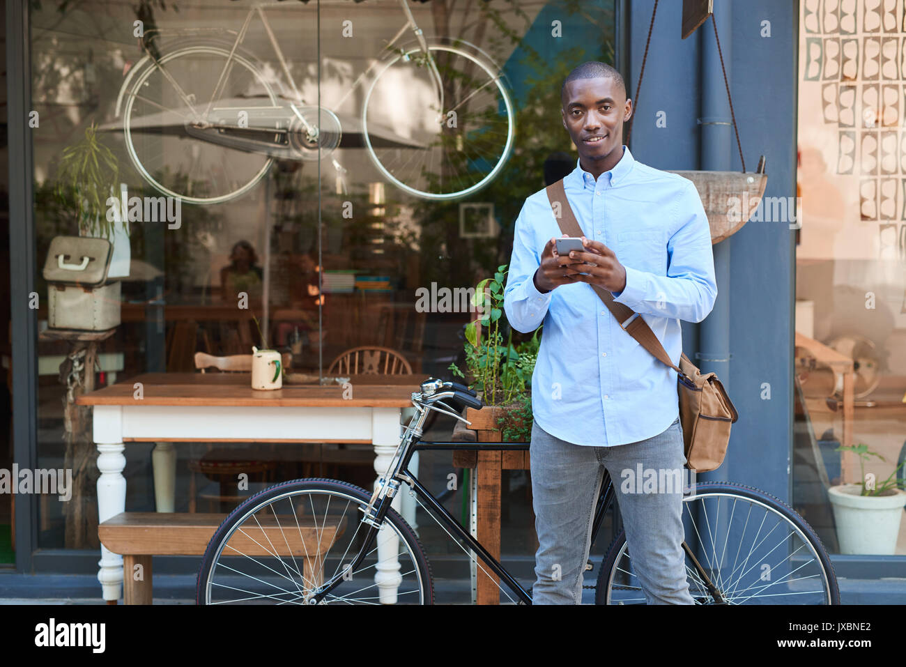 Sorridente giovane uomo in piedi in strada la lettura di messaggi di testo Foto Stock