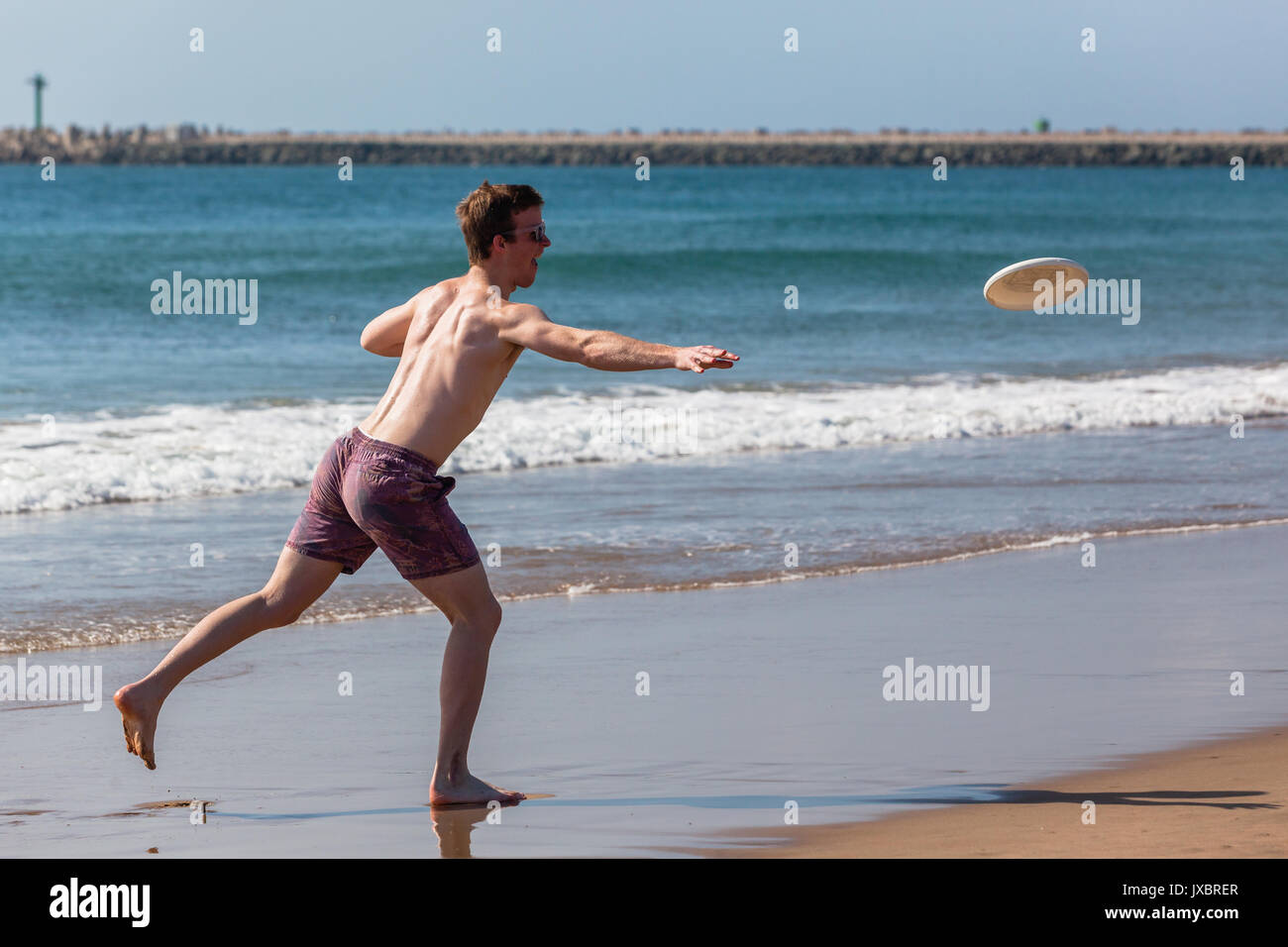 Gli adolescenti boy lanciando Frisby su beach ocean linea di galleggiamento. Foto Stock