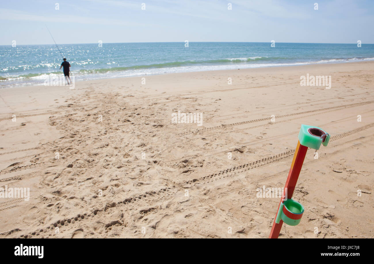 Il pescatore pesca sulla spiaggia con asta di supporto sul primo piano. La pesca con lenza in mare sport in spiaggia, Huelva, Spagna Foto Stock